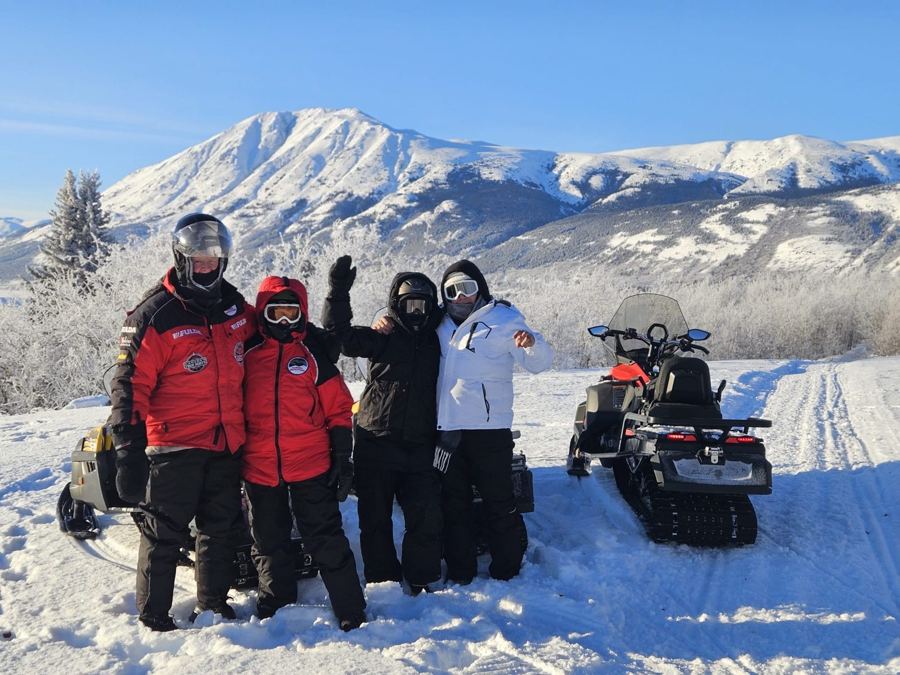 Groupe en motoneige posant face aux montagnes