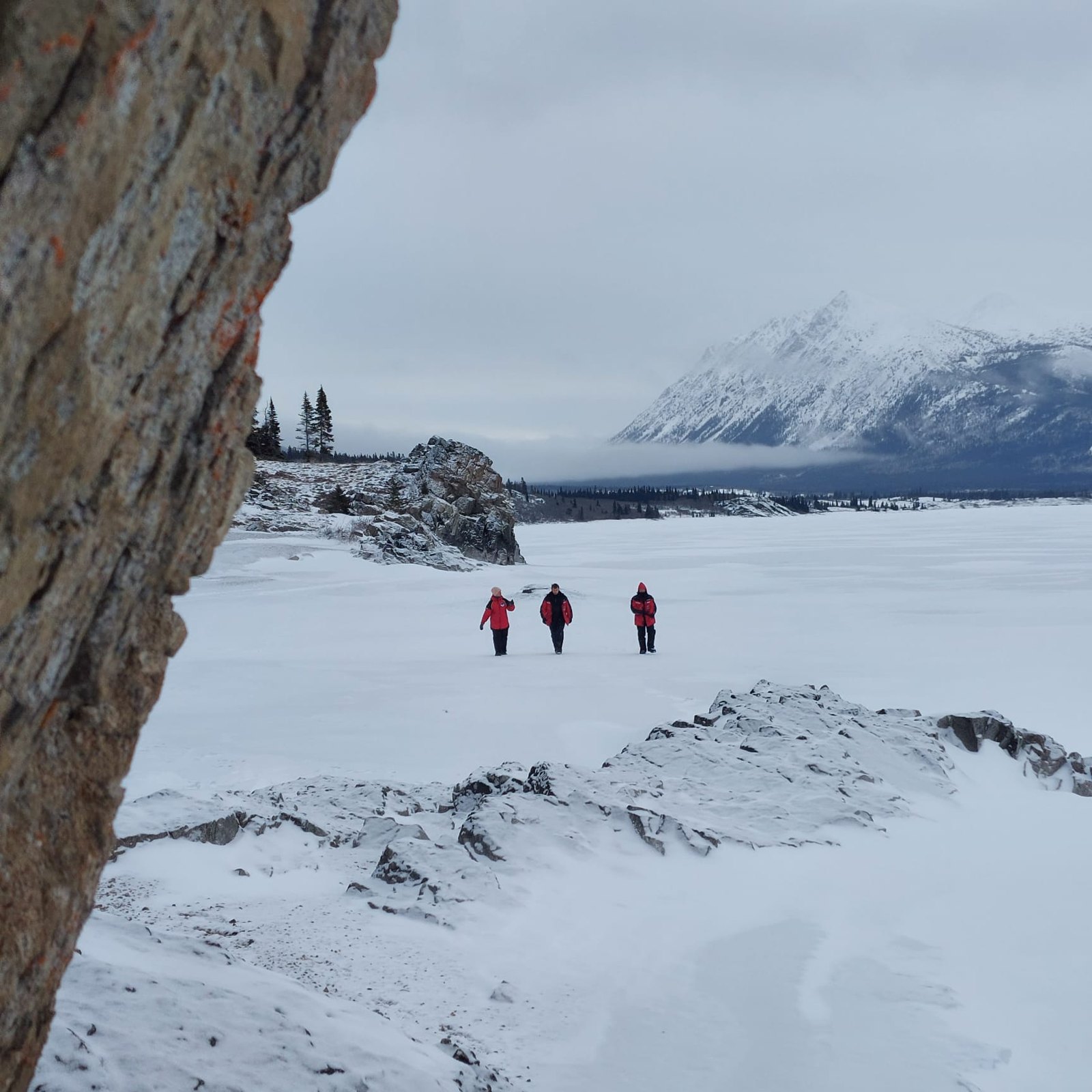 Trois voyageurs marchent sur un lac gelé, face aux montagnes